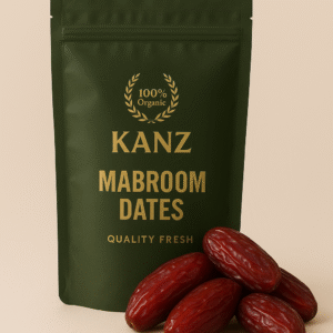 Home Premium Kanz Mabroom Dates in a resealable dark green pouch with gold branding. Long, naturally glossy Mabroom dates with a deep reddish-brown shine are arranged in front, highlighting their distinctive elongated shape and fresh, high-quality appearance against a soft beige background.